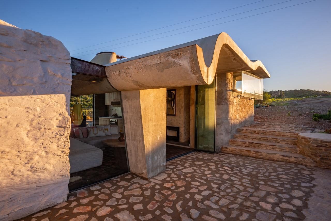 Sheep Herder's Cottage — freeform concrete shell roof glowing at dusk over lime-washed stone