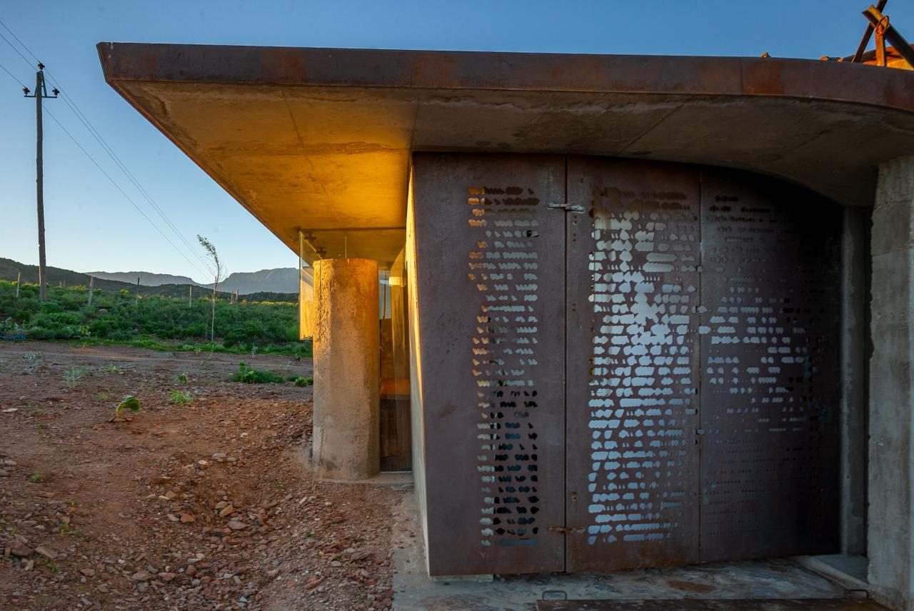 Buffelsdrift sheep herder's cottage — laser-cut steel door, concrete slab, dusk